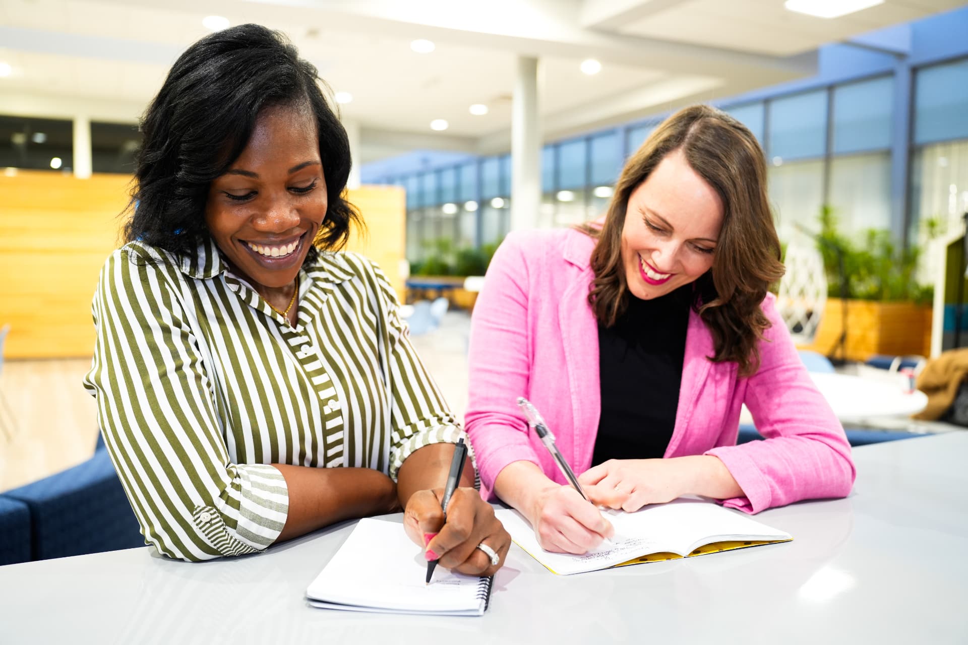 Andronique and Robin smiling and working together taking notes with pen and paper.